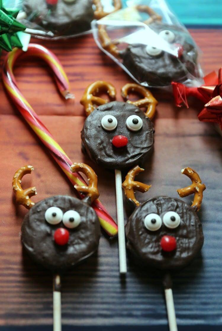 How to Make Reindeer Christmas Cookie Pops 20 Reindeer Christmas Cookie Pops laying on table with cancy cane and bows