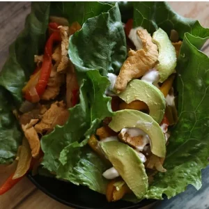 Delicious One Pan Chicken Fajita-ish Wraps: Beat The Diet Tax 17 A close up overhead shot of a healthy chicken fajita lettuce wrap loaded with peppers and onions, topped with source cream and avocados. Half Baked Media
