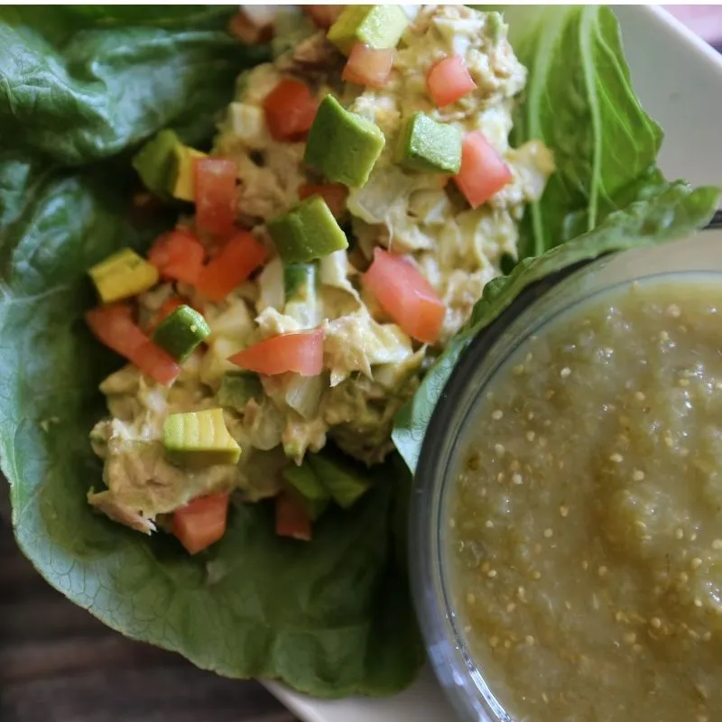 The Ultimate Avocado Tuna Salad Wrap (High-Protein & Low Calorie Lunch) 11 close up on fresh avocado tuna salad wrap on green piece of crispy lettuce next to a bowl of salsa verde