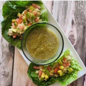 The Ultimate Avocado Tuna Salad Wrap (High-Protein & Low Calorie Lunch) 17 Close-up of two fresh avocado tuna salad wraps arranged on a white plate with a small bowl of salsa verde in the center.