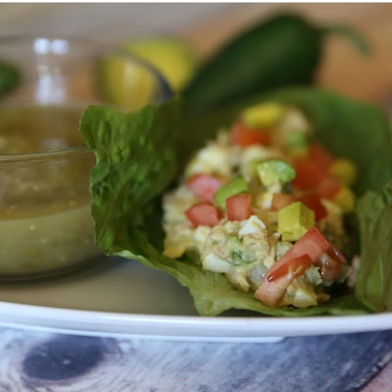 The Ultimate Avocado Tuna Salad Wrap (High-Protein & Low Calorie Lunch) 15 Close up of tuna lettuce wrap with diced avocado and tomato on top beside a glass bowl of salsa verde.