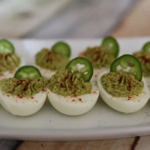 Holy Guacamole Deviled Eggs garnished with jalapeno slice and smoked paprika on a white plate