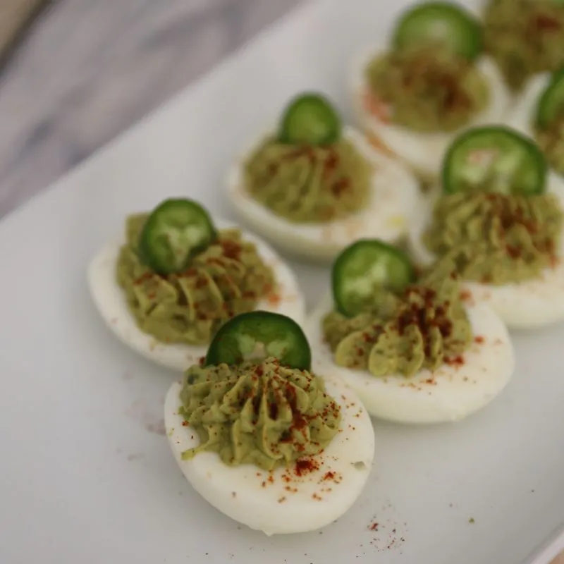 Holy Guacamole Deviled Eggs garnished with jalapeno slice and smoked paprika on a white plate
