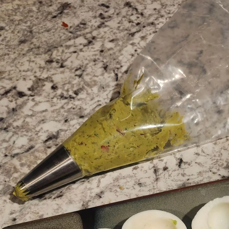 poping back filled with Holy Guacamole Deviled Eggs filling ready to be piped into eggs.
