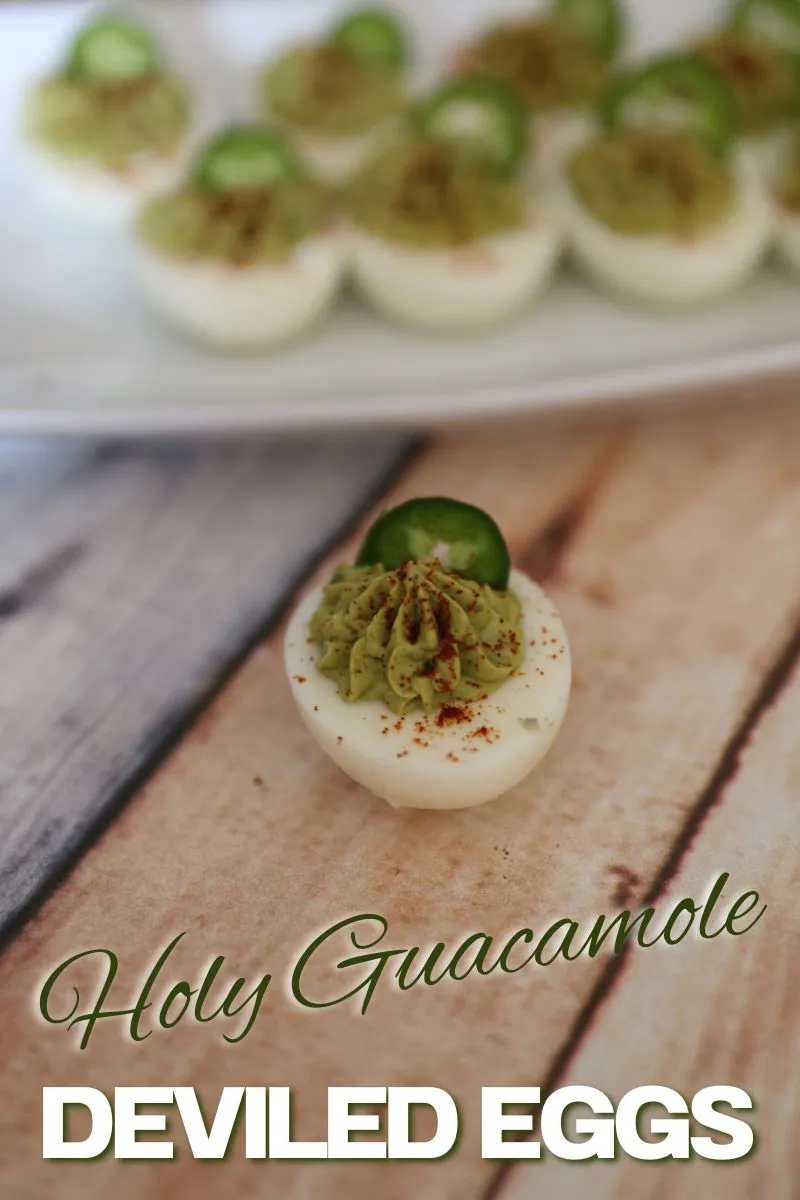 Holy Guacamole Deviled Eggs on a white plate garnished with jalapeno, one deviled egg is sitting on the table.