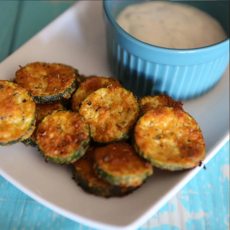 Baked Parmesan Zucchini on long white plate with blue bowl filled with ranch dressing