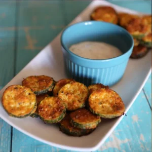 Baked Parmesan Zucchini on white plate with ranch in the center in blue bowl on rustic blue wooden table