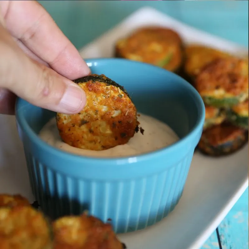 hand holding and dipping Baked Parmesan Zucchini in ranch dressing
