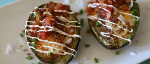 Loaded Southwest Baked Avocado Egg Boats on white plate with sour cream drizzled over the top