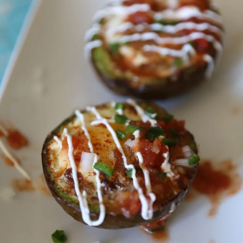 Loaded Southwest Baked Avocado Egg Boats on white plate topped with jalapeno, onion and sour cream.