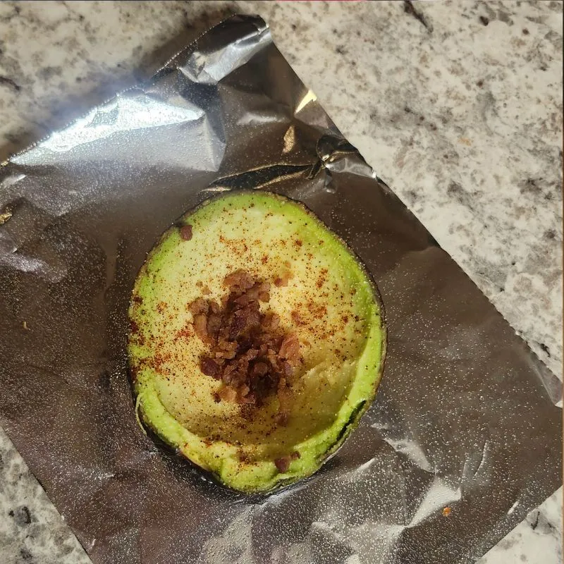 avocado half on foil with bacon bits in the center.