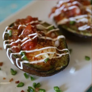 Loaded Southwest Baked Avocado Egg Boats topped with sour cream, diced jalapeno and onion on a white plate