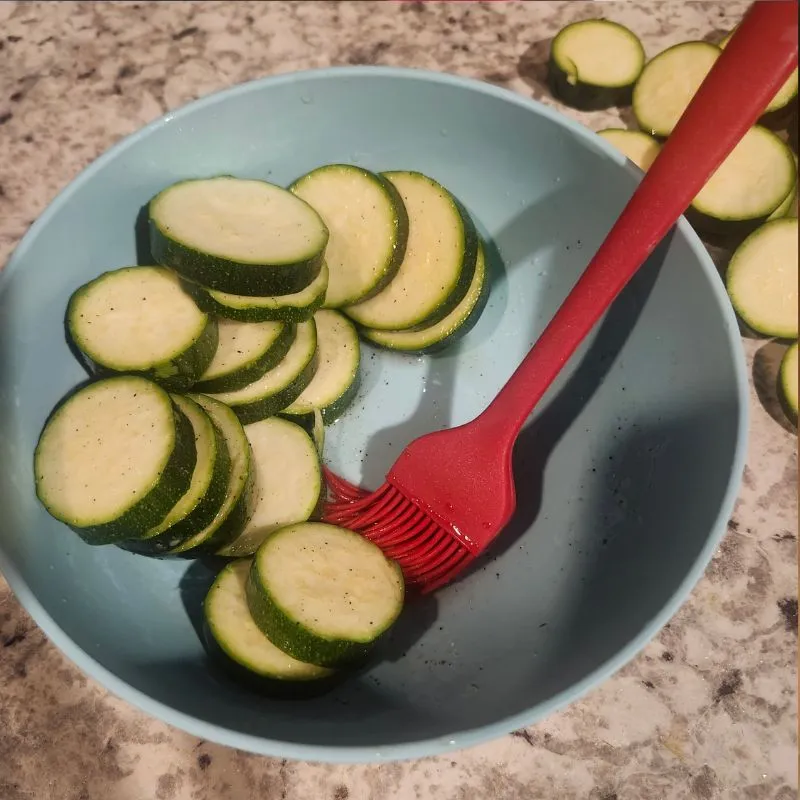 parmesan zucchini in bowl being covered in olive oil mixture