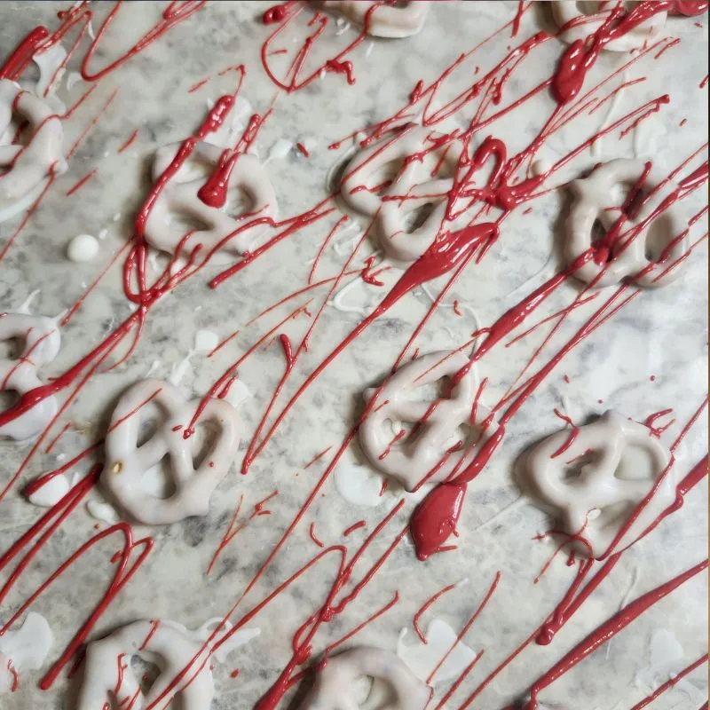 pretzels dipped in white chocolate spattered with red candy melts to look like blood drying on parchment paper.