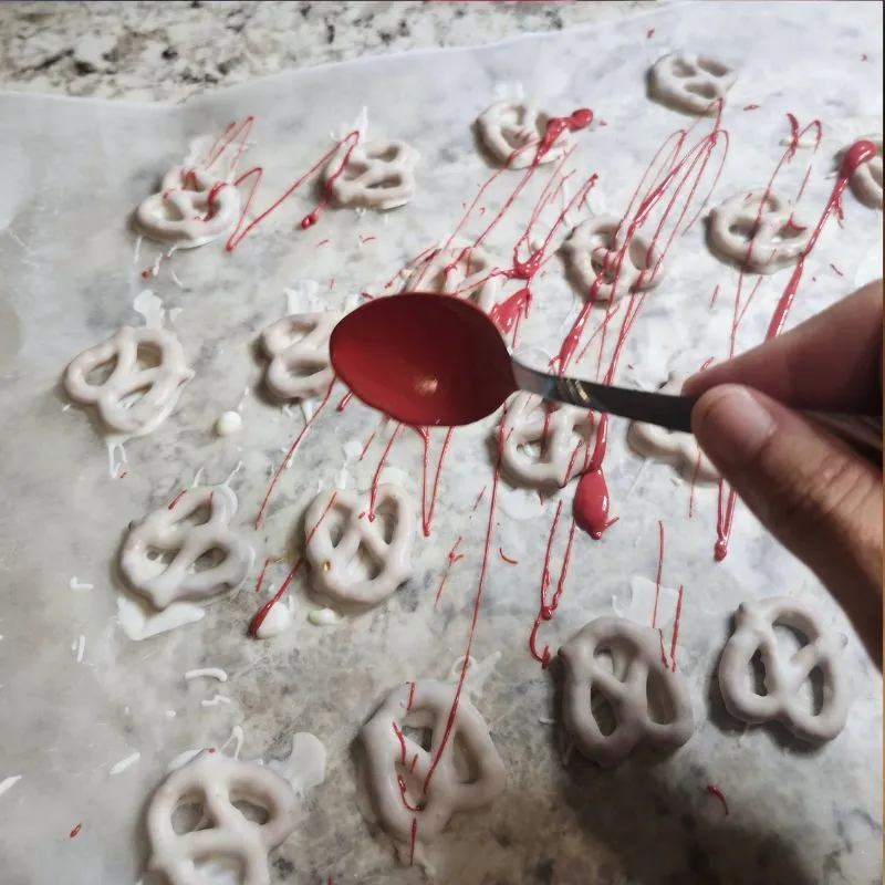 Using a spoon to spatter pretzels covered in white chocolate with red candy melts