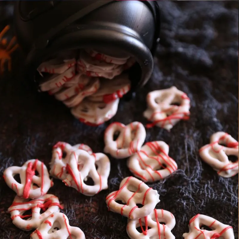 A festive dish of crunchy twist pretzels dipped in smooth white chocolate and decorated with a splatter of red candy melt "blood" for a spooky Halloween treat.