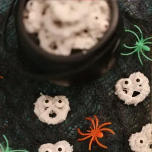 White chocolate mummy pretzels with candy eyes, arranged in and around a black cauldron on a spooky Halloween background.