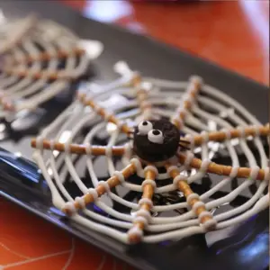 Easy Halloween Treats No-Bake Oreo Pretzel Spider Webs sitting on a place plate with an orange background