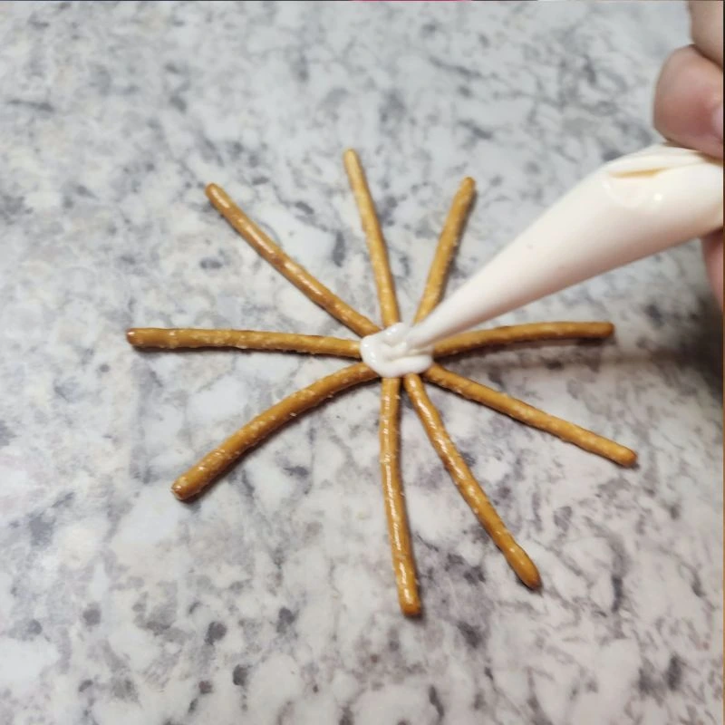 Piping melted white chocolate over the center of the pretzel star on wax paper.