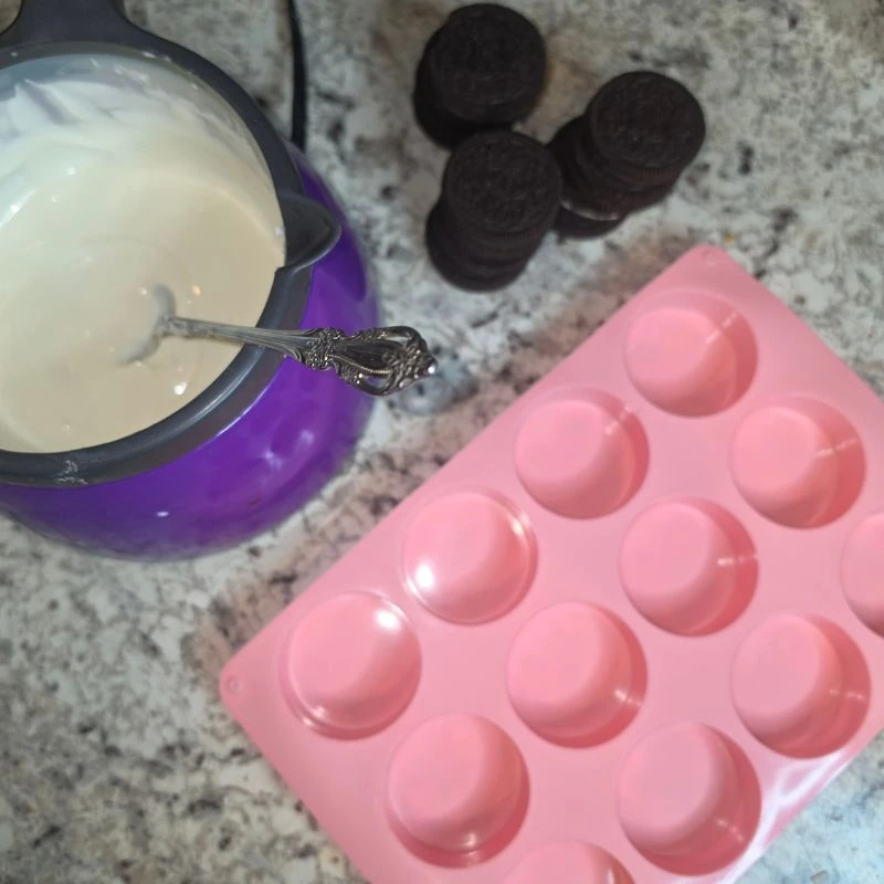 Almond bark melted in melting pot with oreo cookies and pink mold sitting next to it