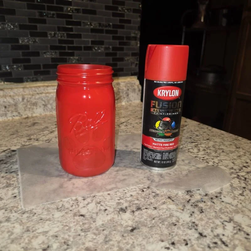 Awesome DIY Dog Treat Jar Using a Mason Jar 16 mason jar spary painted red with homemade paw print sticker sitting on counter next to can of red spray paint
